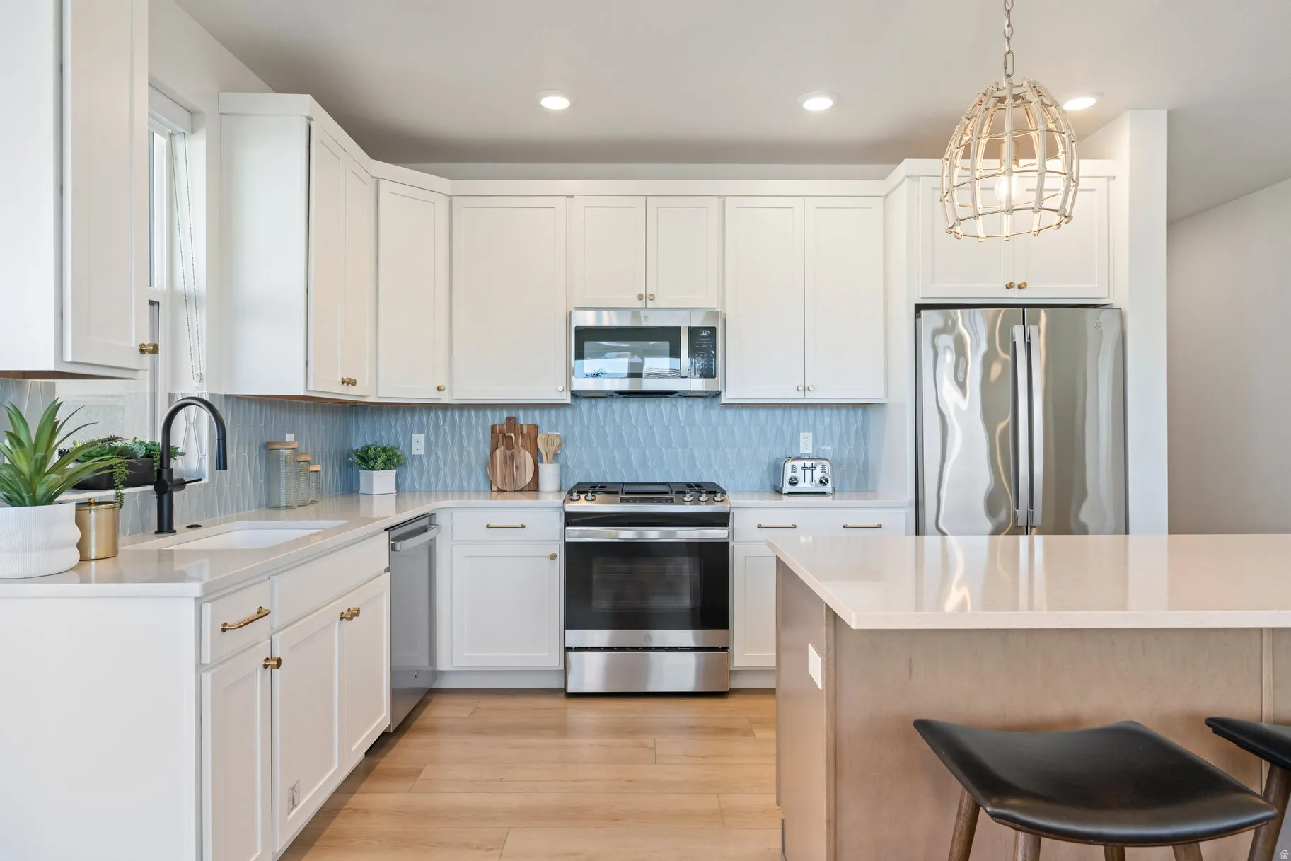 Kitchen with stainless steel appliances, white cabinets, light wood finished floors, light stone countertops, and decorative light fixtures