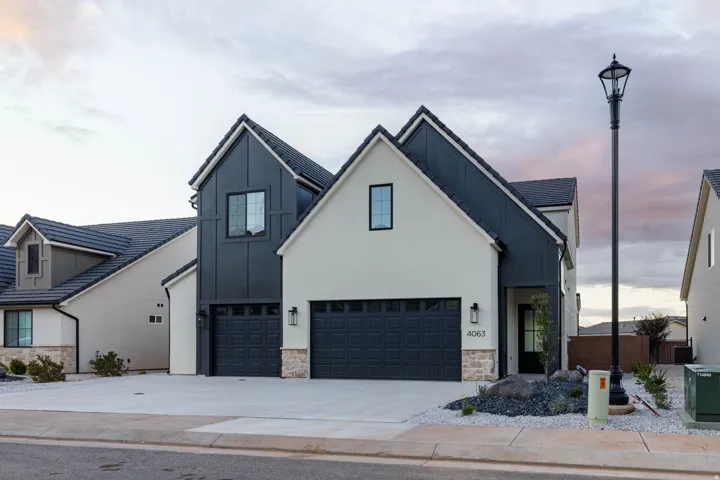 Modern farmhouse style home with stone siding, driveway, board and batten siding, and a garage