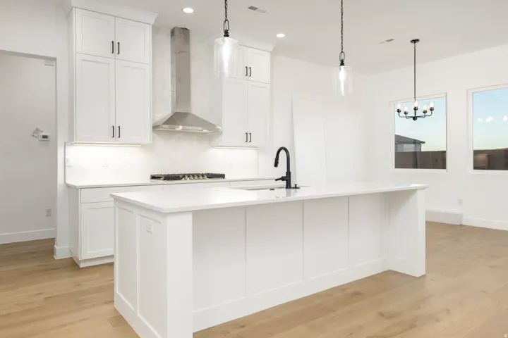Kitchen featuring wall chimney range hood, white cabinetry, decorative light fixtures, decorative backsplash, and light wood-type flooring