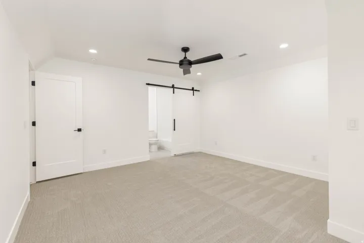 Unfurnished bedroom with recessed lighting, a barn door, ceiling fan, light colored carpet, and ensuite bathroom