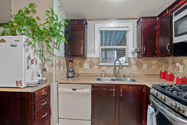 Kitchen with stainless steel appliances, light countertops, a textured ceiling, tasteful backsplash, and dark brown cabinets