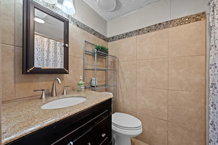 Full bath with a textured ceiling, a shower with curtain, vanity, and tile walls