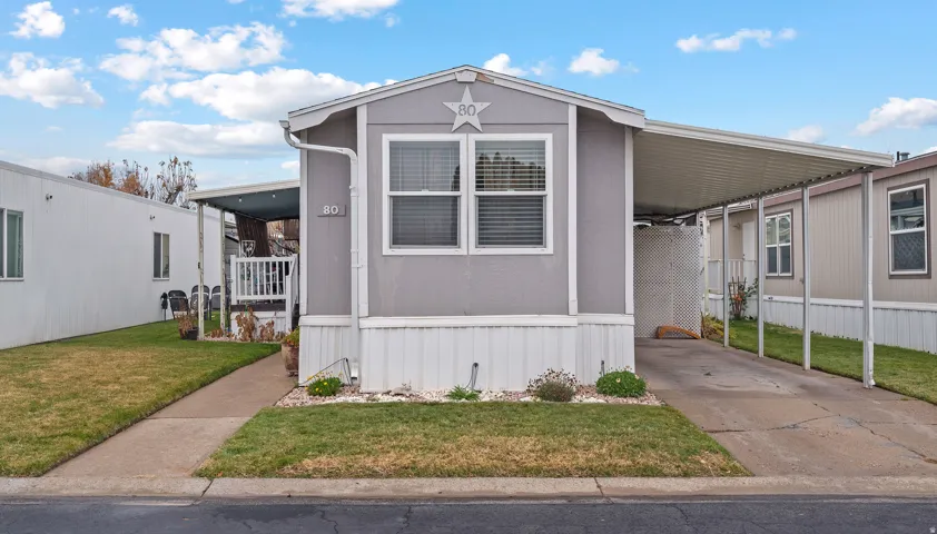 Manufactured / mobile home with a front lawn, an attached carport, concrete driveway, and a porch