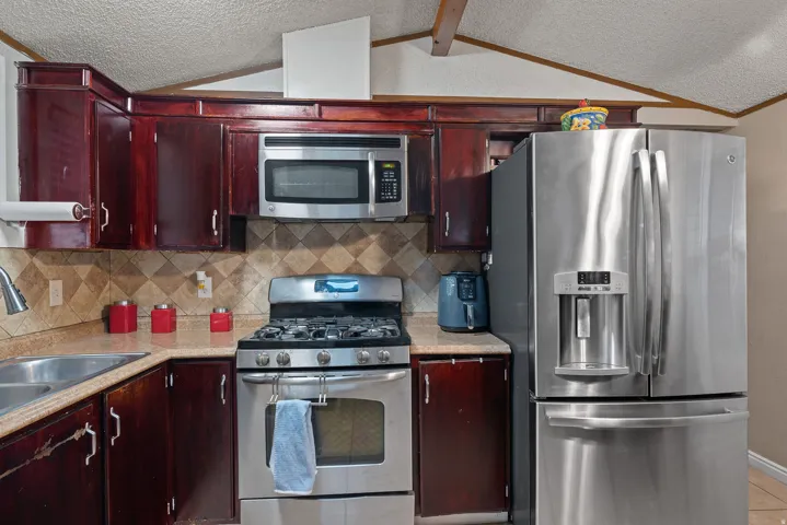 Kitchen with appliances with stainless steel finishes, decorative backsplash, light countertops, a textured ceiling, and lofted ceiling