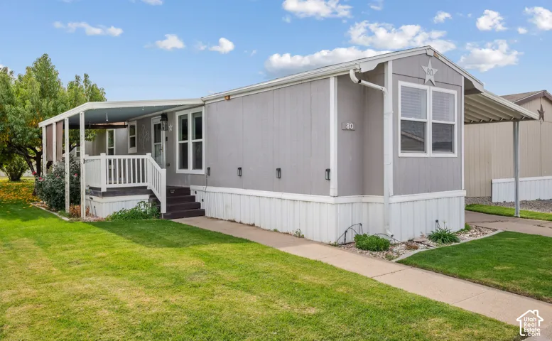 Exterior featuring light grey siding, a covered porch with white railing, a side carport, and a concrete walkway