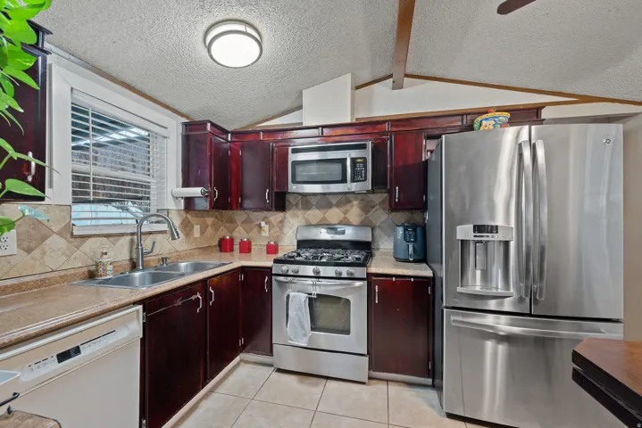 Kitchen with stainless steel appliances, light countertops, backsplash, lofted ceiling, and light tile patterned flooring