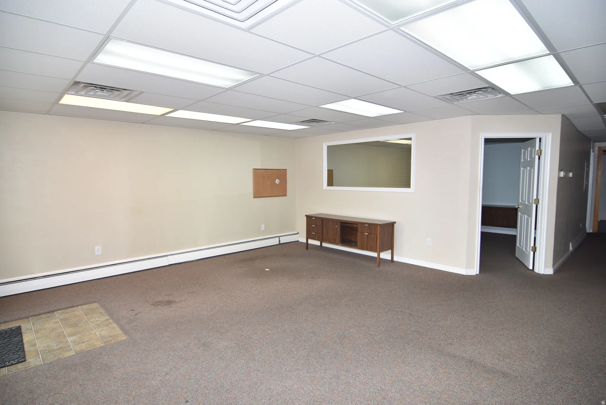 Unfurnished room featuring baseboard heating, carpet, and a drop ceiling
