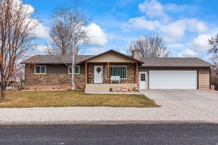 Ranch-style home with concrete driveway, stone siding, covered porch, a front lawn, and an attached garage