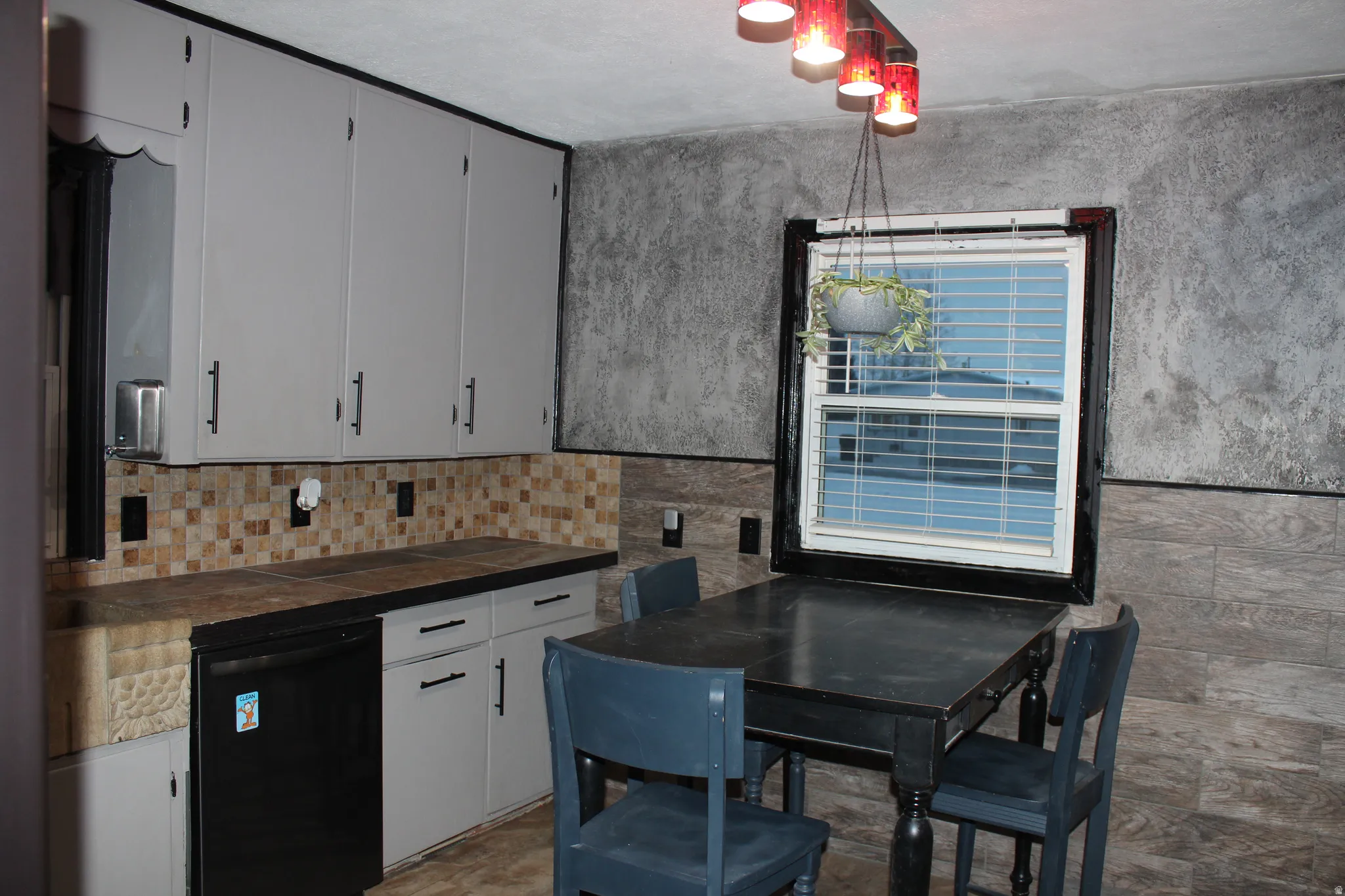 Kitchen with black dishwasher, white cabinetry, tile counters, tasteful backsplash, and tile walls