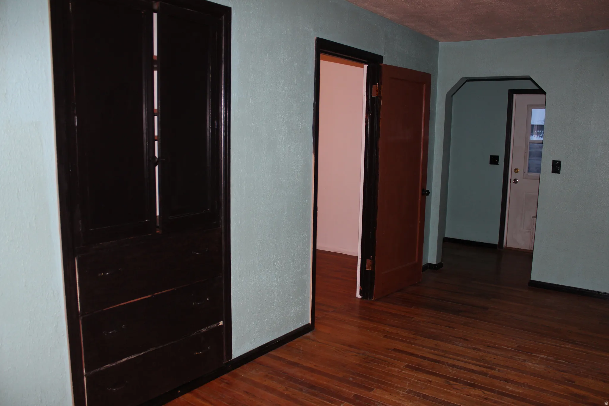 Hall with arched walkways, dark wood-style floors, and a textured wall