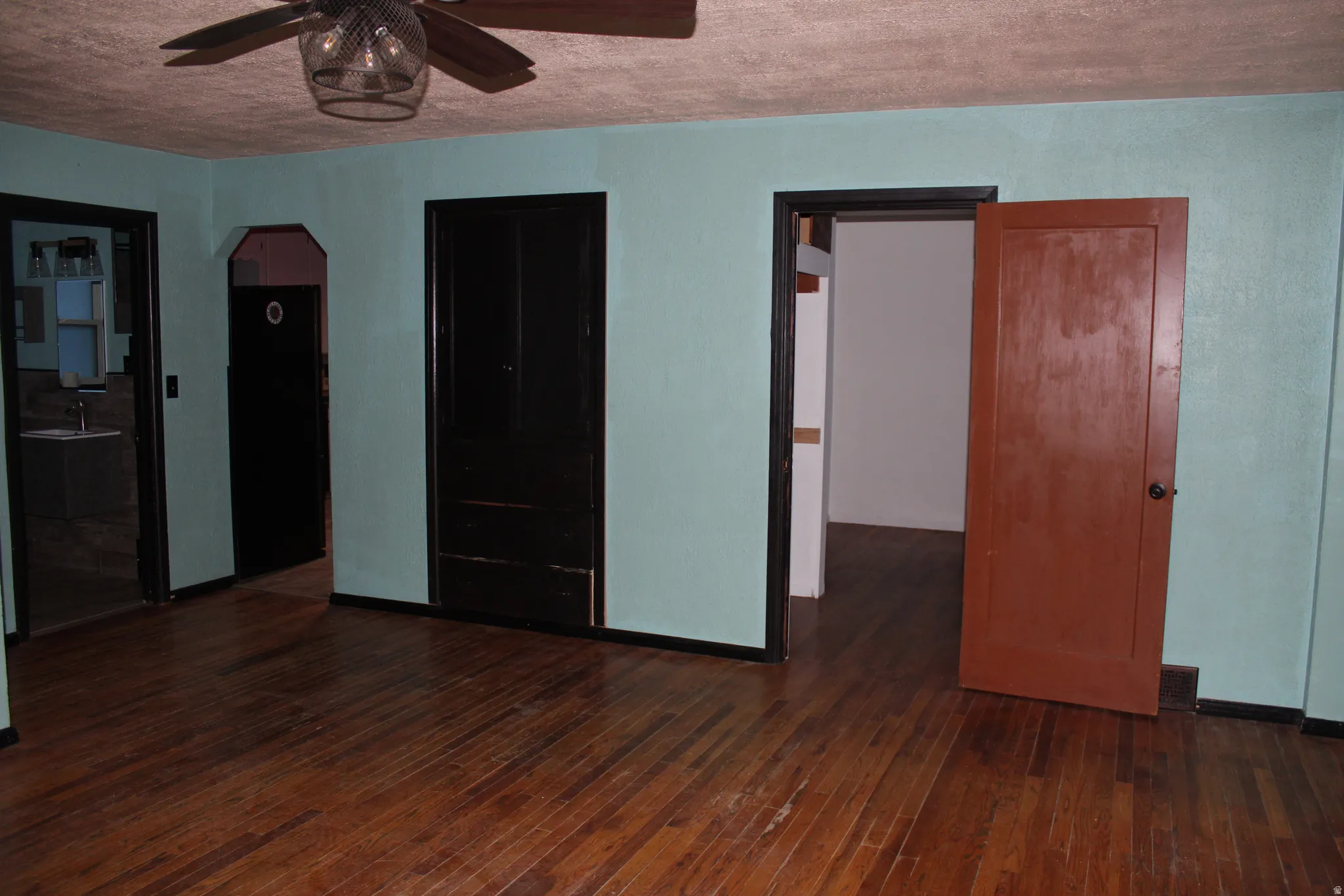 Unfurnished bedroom featuring dark wood-style flooring, arched walkways, a ceiling fan, and a textured ceiling