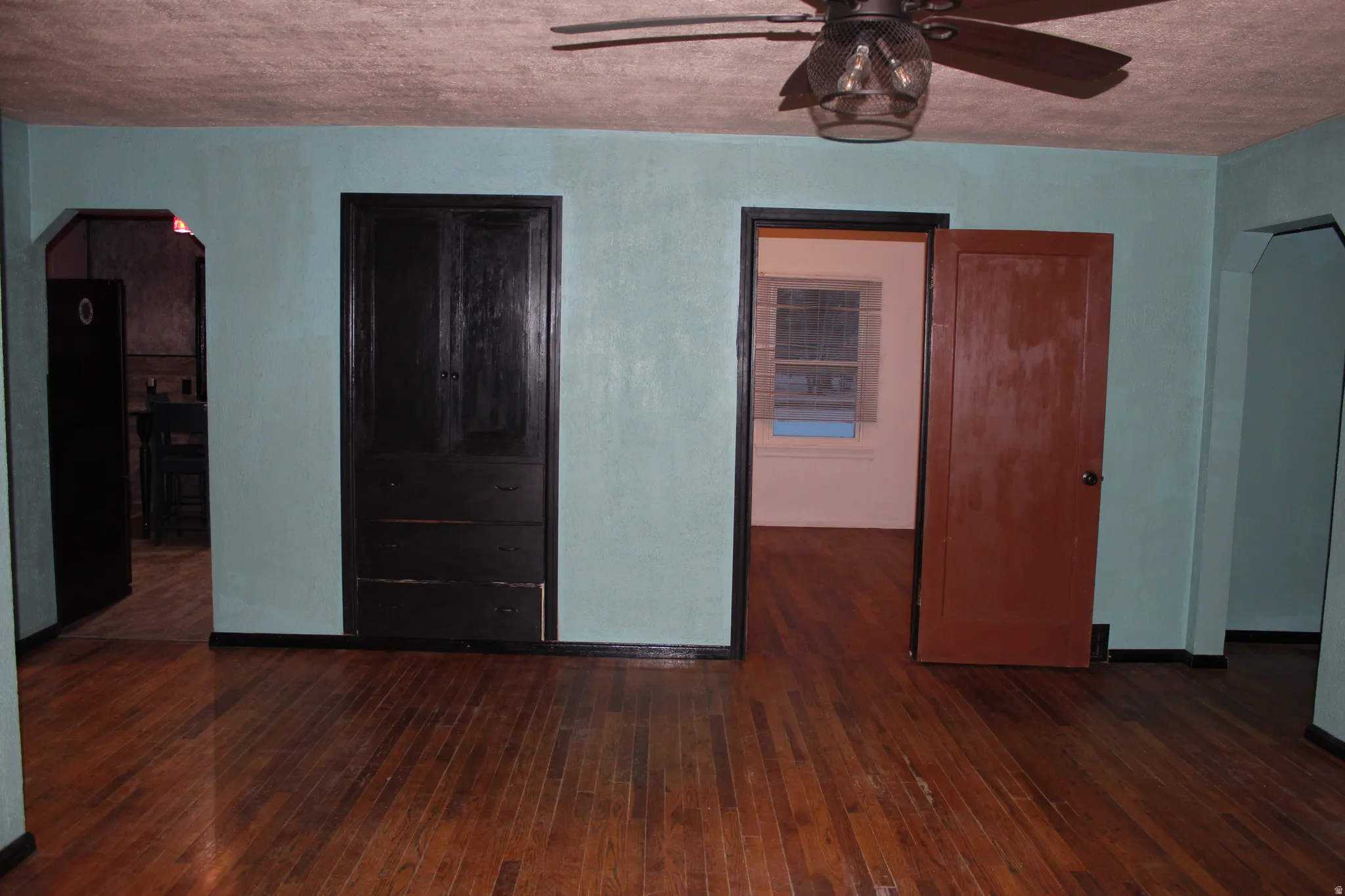 Unfurnished room with arched walkways, dark wood-style flooring, a textured ceiling, and a ceiling fan