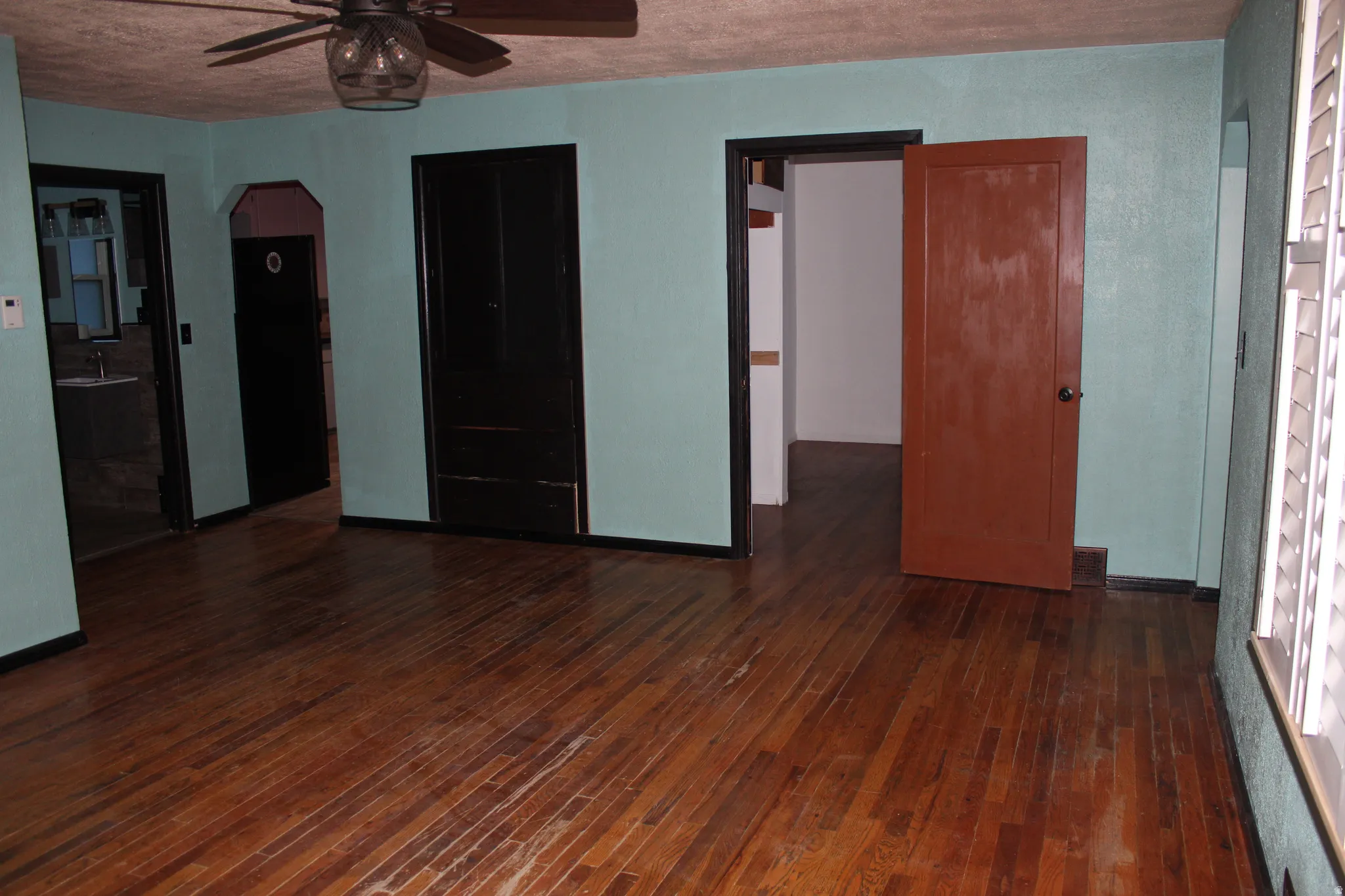 Unfurnished room with arched walkways, dark wood-type flooring, and a ceiling fan