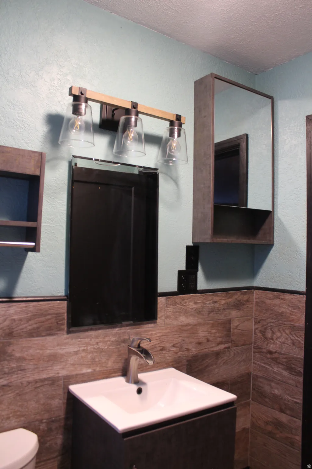 Half bathroom with a textured wall, vanity, a wainscoted wall, a textured ceiling, and tile walls