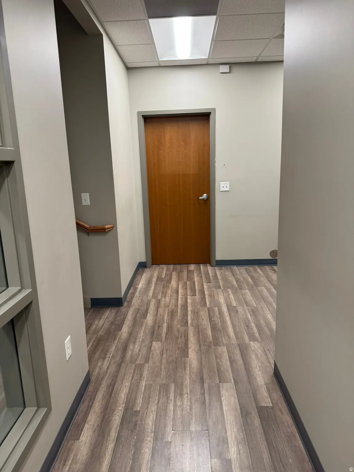 Corridor with a drop ceiling and wood finished floors
