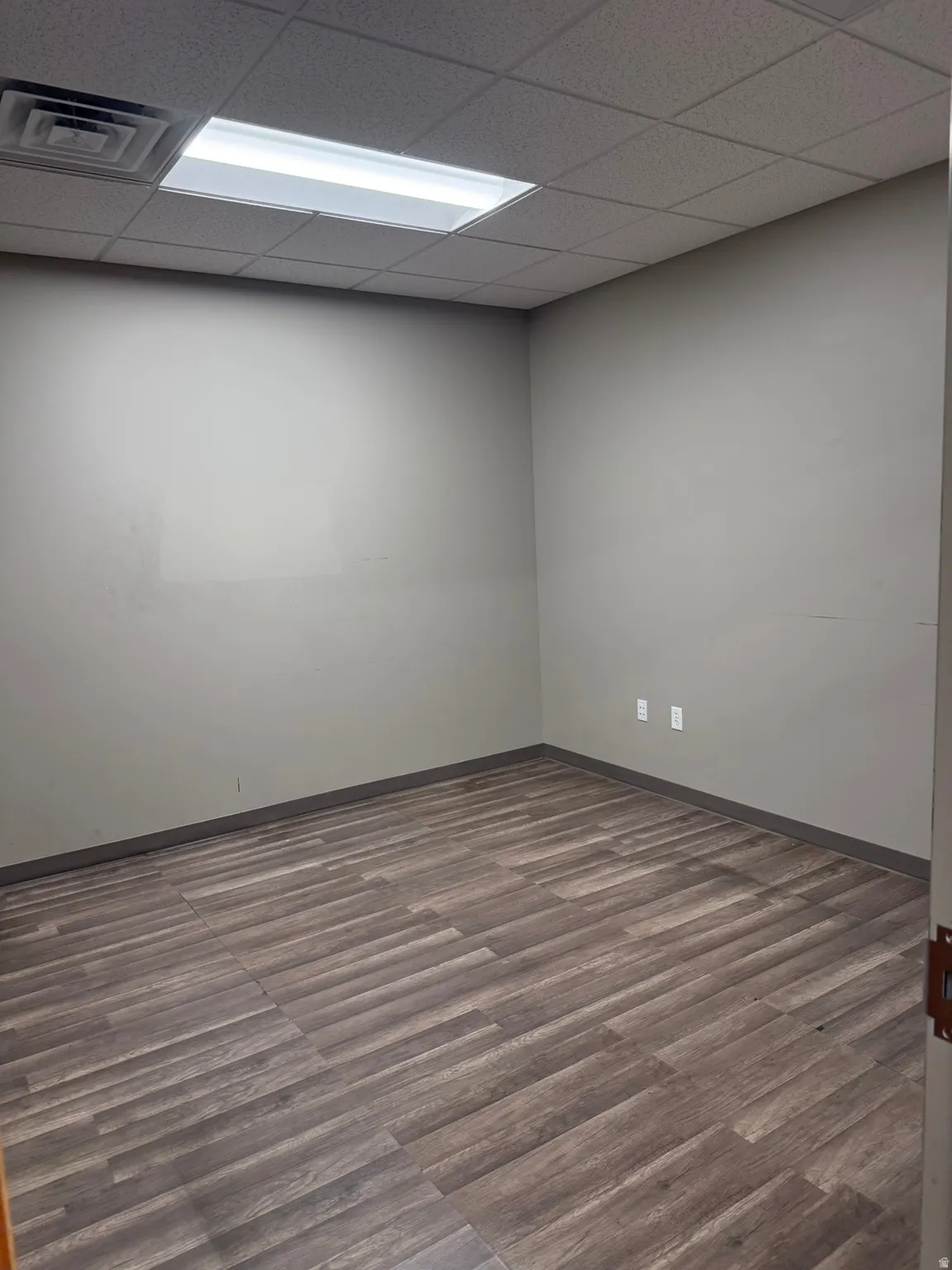 Empty room featuring a drop ceiling and dark wood-style flooring