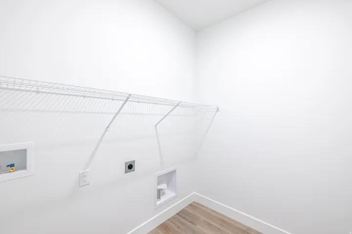 Dedicated laundry space featuring white walls, wire shelving, wood-finish flooring, and essential utility hookups