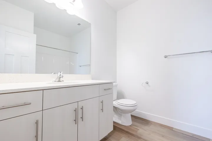 Bathroom featuring a light wood-finish vanity with ample storage, a white countertop, a wide mirror, and bright overhead lighting