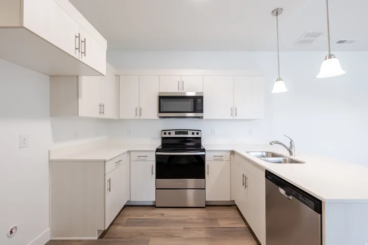 Modern kitchen featuring white cabinetry, light-toned countertops, stainless steel appliances, and wood-finish flooring