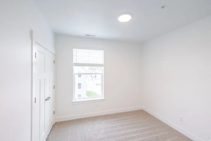 Neutral-toned carpeting extends throughout this room, featuring a window with integrated blinds