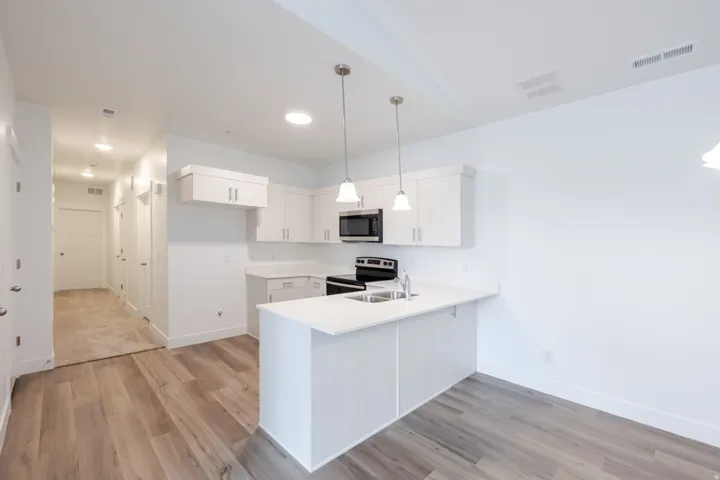 Modern kitchen featuring white cabinetry, light countertops, stainless steel sink, and pendant lighting