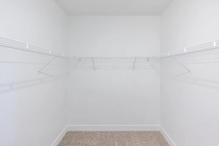 Walk-in closet featuring white wire shelving, white baseboards, and neutral carpet flooring