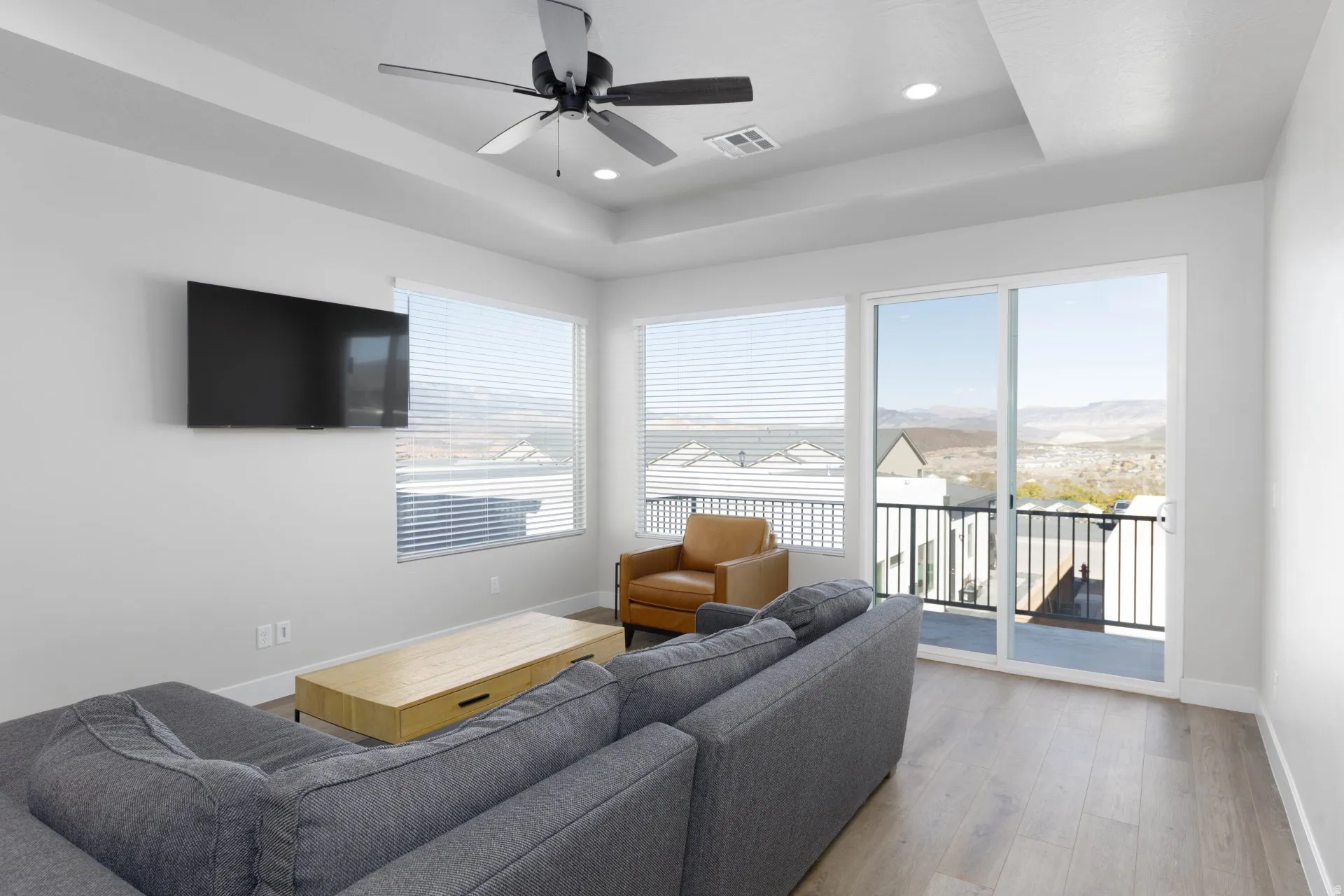 Living room with a raised ceiling, ceiling fan, wood finished floors, and recessed lighting