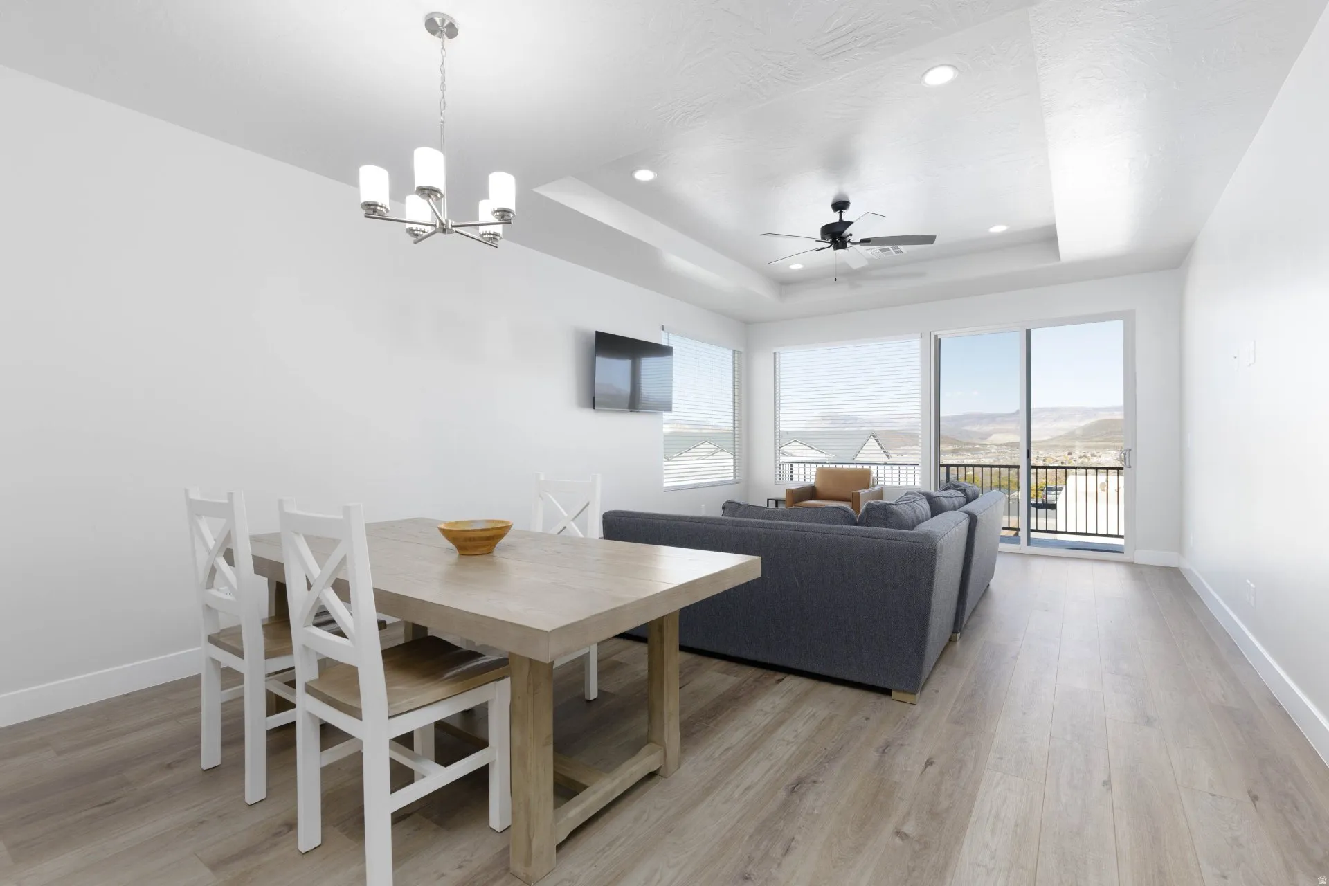 Dining room with light wood-style flooring, a raised ceiling, ceiling fan, recessed lighting, and a chandelier