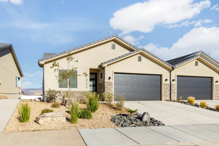 View of front facade with stone siding, stucco siding, driveway, and a garage
