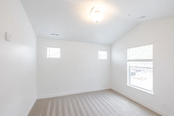 Vaulted ceiling room featuring light beige carpet, white baseboards, and four windows for natural light
