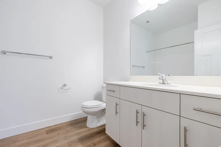 Bathroom featuring wood-finish flooring, a white vanity with brushed nickel hardware, a rectangular mirror, a white countertop, and a toilet