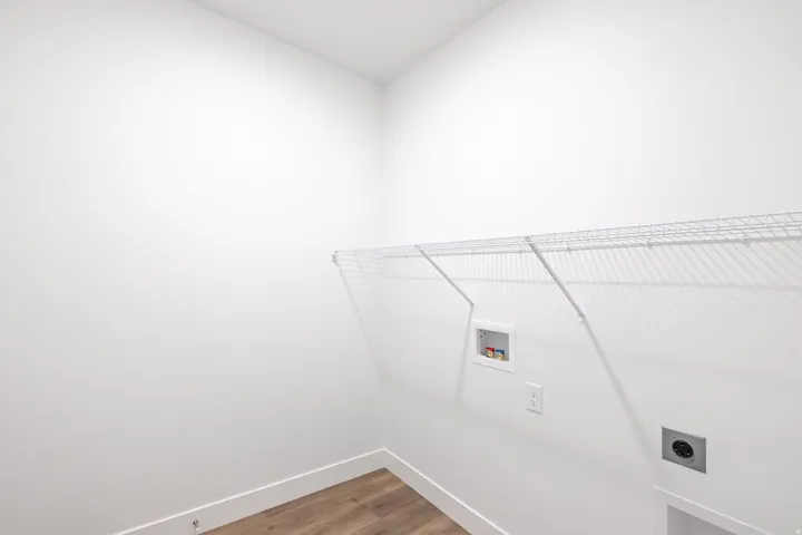 Utility room featuring a wire storage shelf, wall outlet, and plumbing hookups