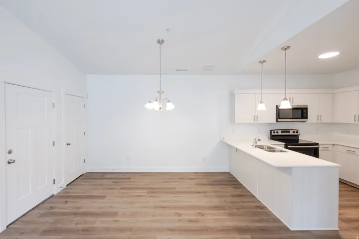 Open-concept living space with wood-finish flooring, a contemporary chandelier, and a kitchen featuring white cabinetry, light-colored countertops, and stainless steel appliances including a microwave and range