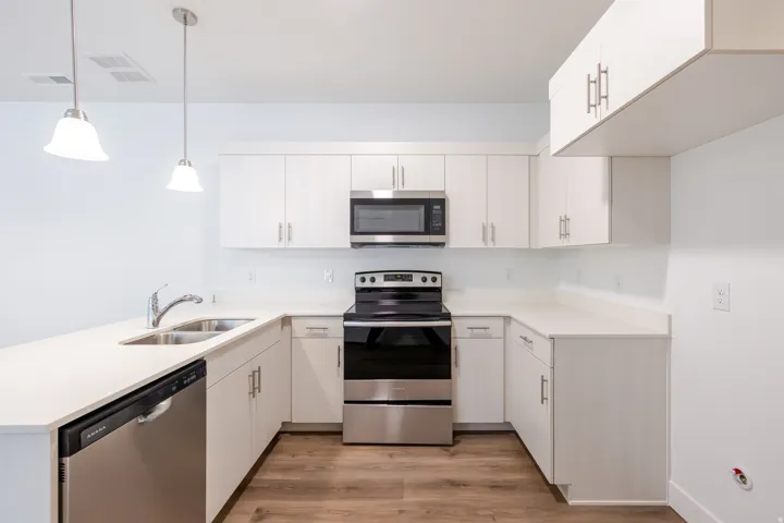 Modern kitchen featuring white cabinetry, light countertops, wood-finish flooring, stainless steel appliances, and pendant lighting