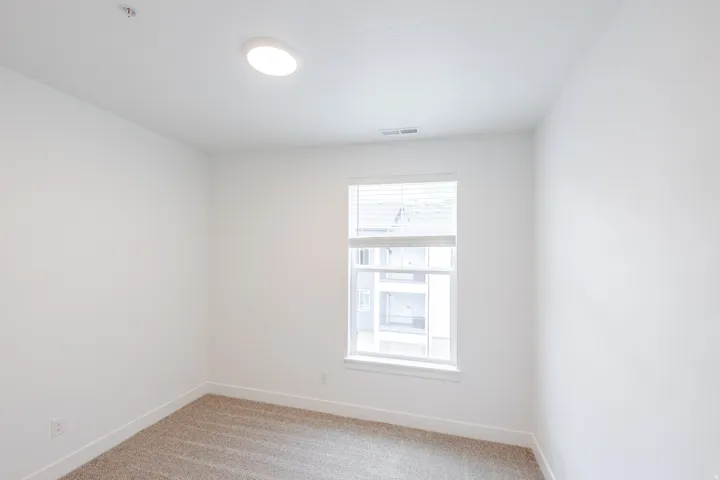 Carpeted room with white walls, a single window featuring horizontal blinds, white baseboards, and a ceiling-mounted light fixture
