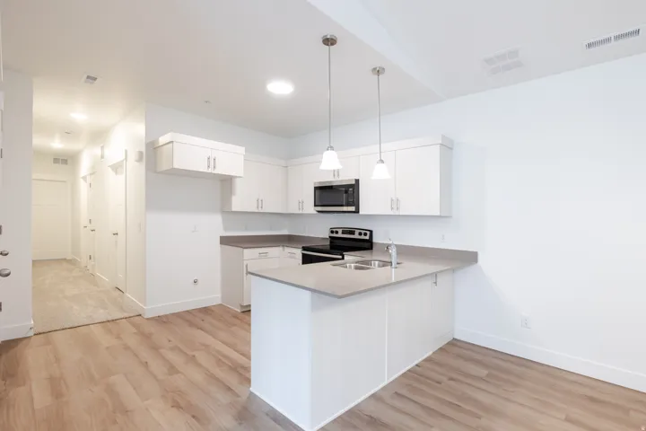 Contemporary kitchen featuring white cabinetry, light countertops, wood-finish flooring, stainless steel appliances, and pendant lighting