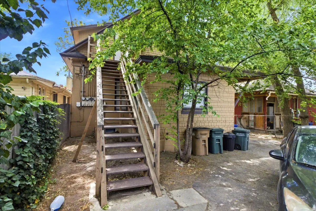 Rear exterior featuring a wood staircase, mature trees, and a paved area