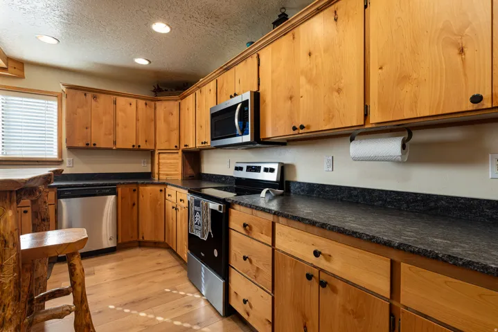 Kitchen featuring stainless steel appliances, a textured ceiling, recessed lighting, dark countertops, and light wood finished floors