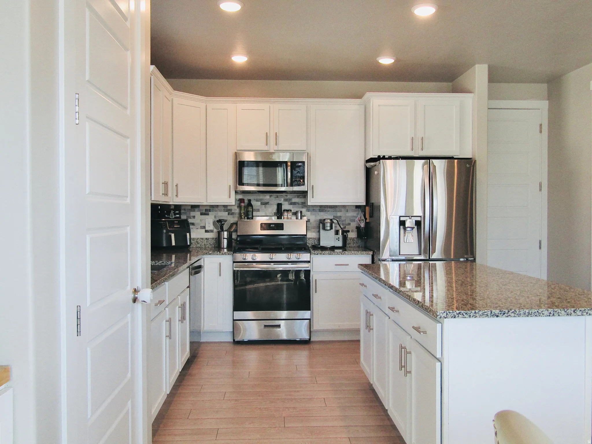 Kitchen featuring appliances with stainless steel finishes, white cabinets, recessed lighting, backsplash, and dark stone counters