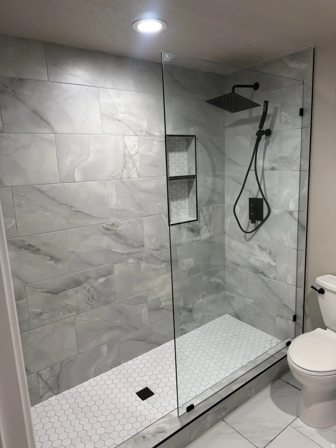 Bathroom featuring walk in shower, light marble finish floors, and recessed lighting