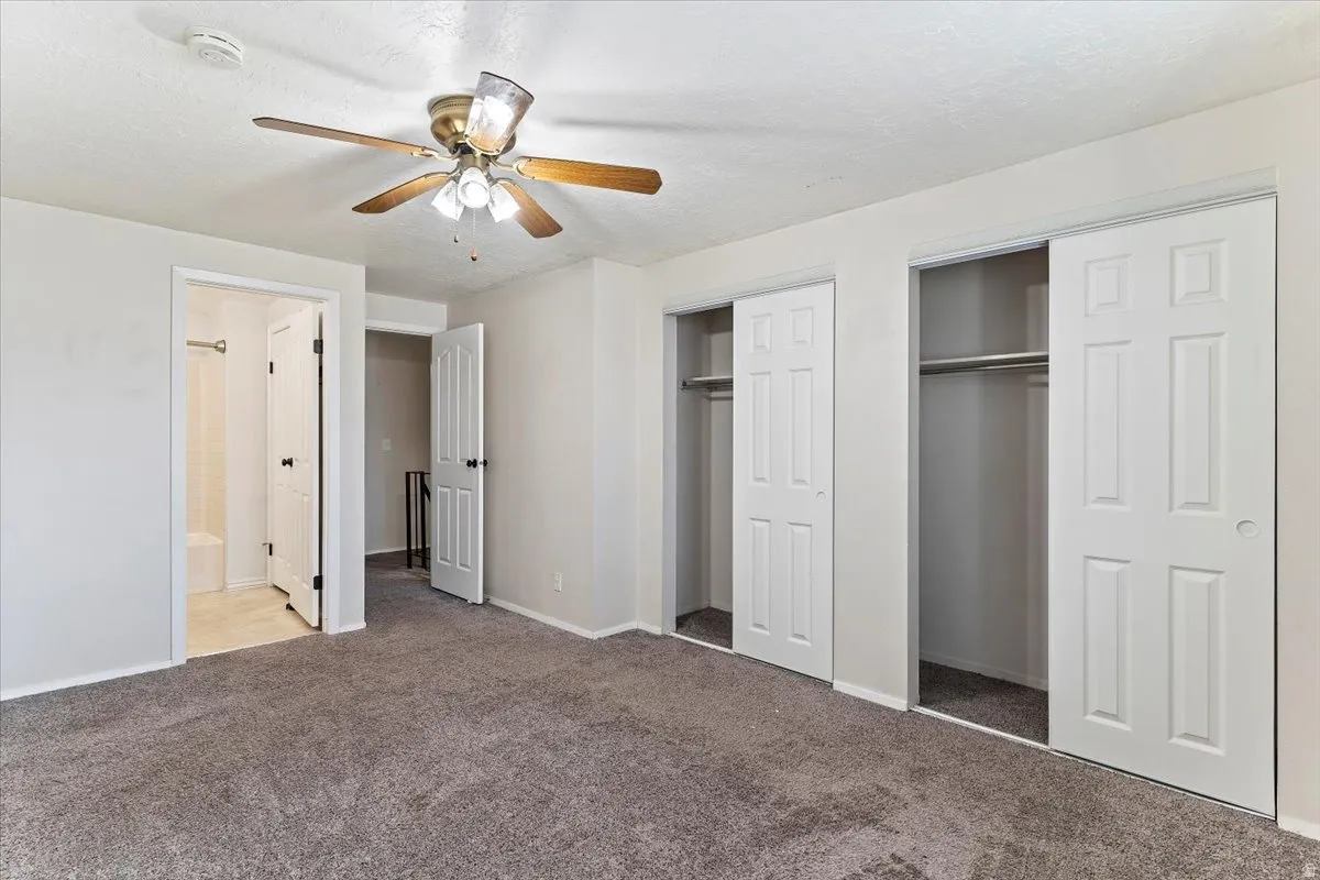Unfurnished bedroom with multiple closets, carpet flooring, a ceiling fan, and a textured ceiling