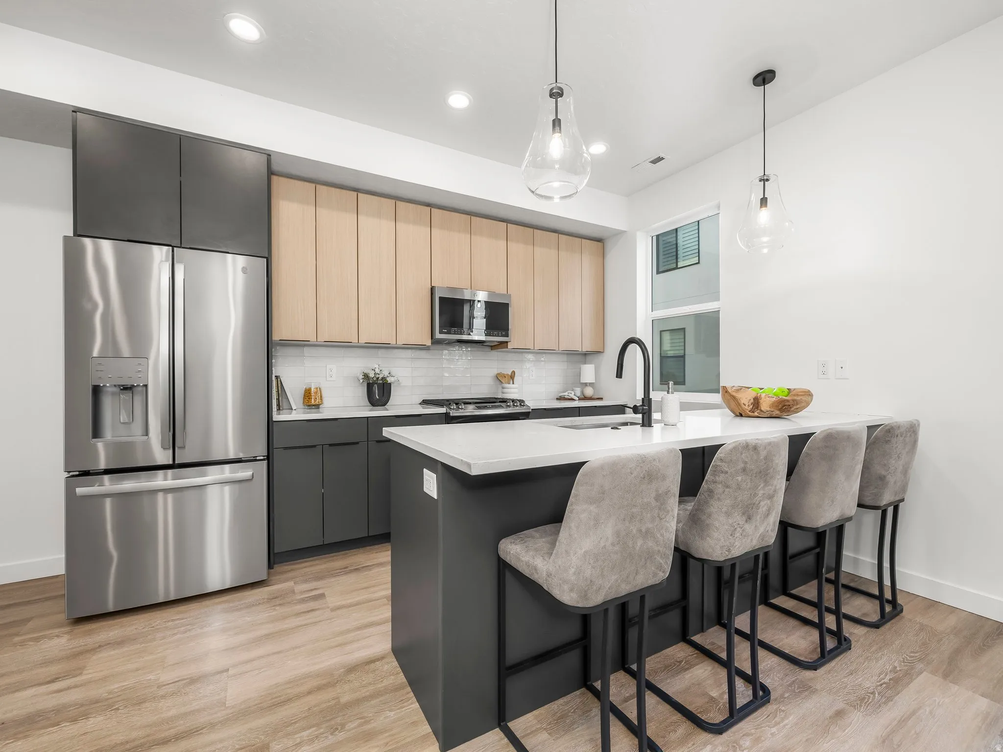 Kitchen with modern cabinets, stainless steel appliances, a peninsula, light brown cabinetry, and hanging light fixtures