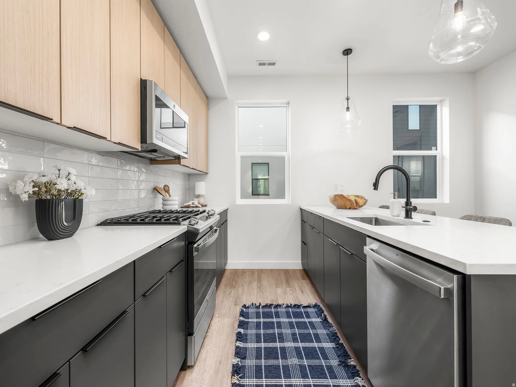 Kitchen with modern cabinets, appliances with stainless steel finishes, pendant lighting, light stone counters, and recessed lighting