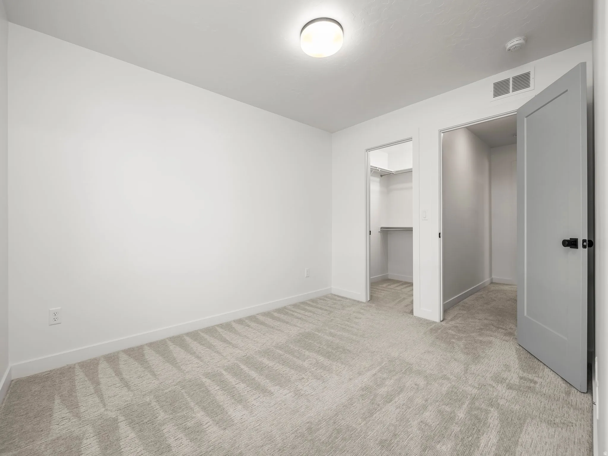 Unfurnished bedroom with light carpet and a walk in closet
