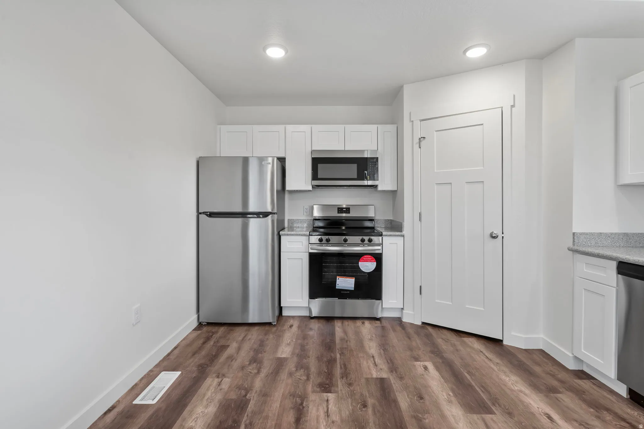 Kitchen with white cabinets, stainless steel appliances, dark wood-style floors, and light stone counters