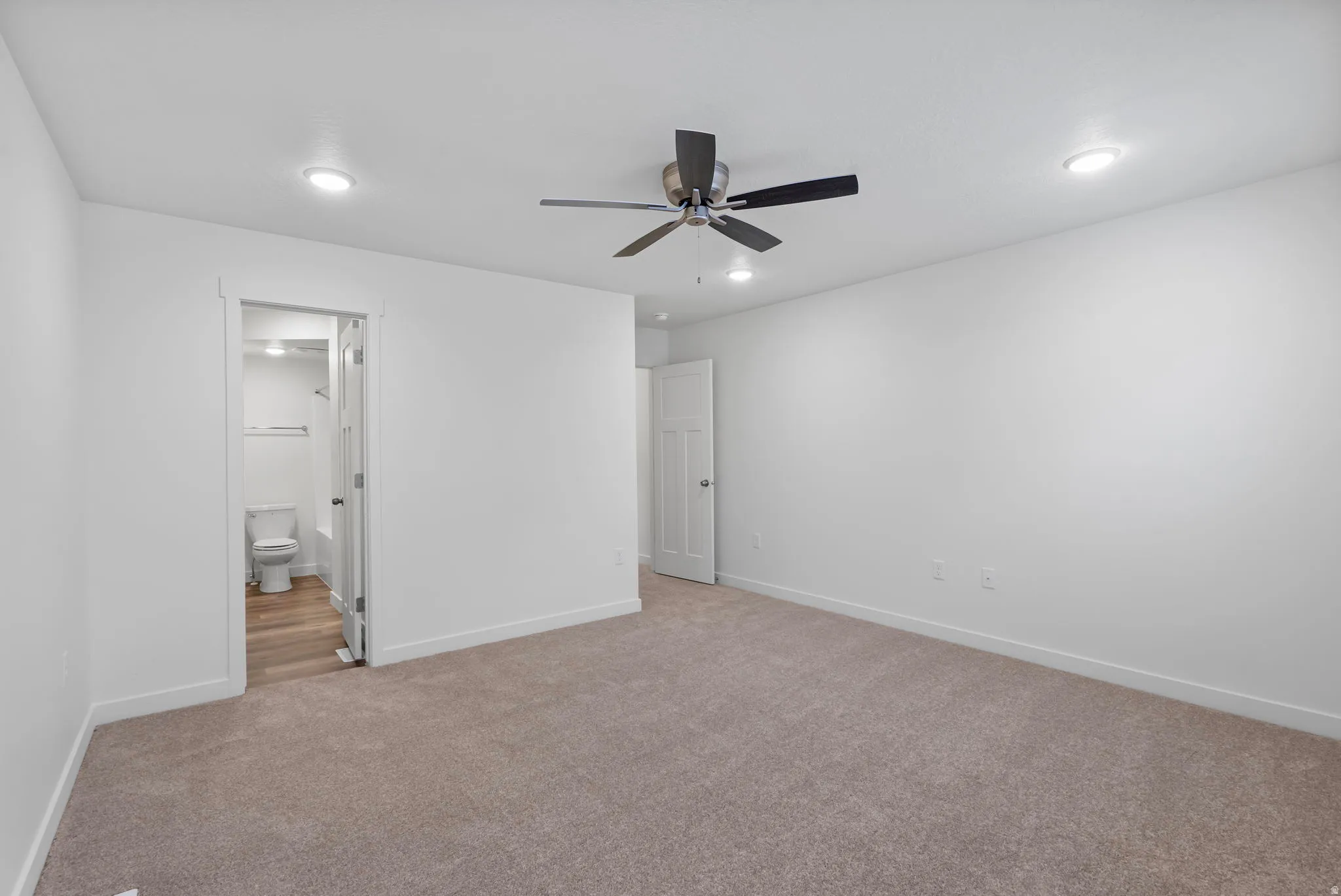 Unfurnished bedroom featuring light colored carpet, a ceiling fan, connected bathroom, and recessed lighting