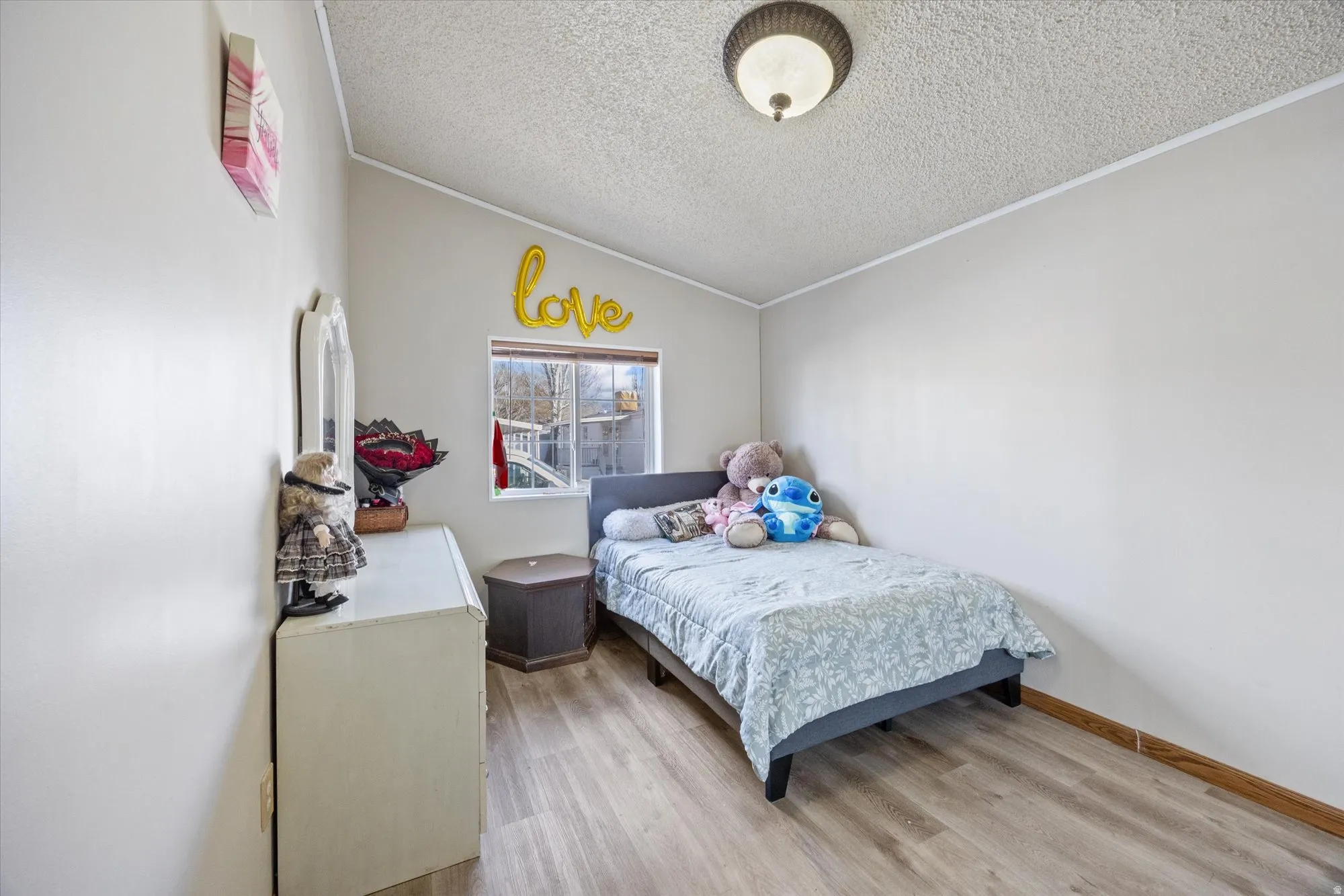 Bedroom featuring vaulted ceiling, light wood-style flooring, a textured ceiling, and crown molding