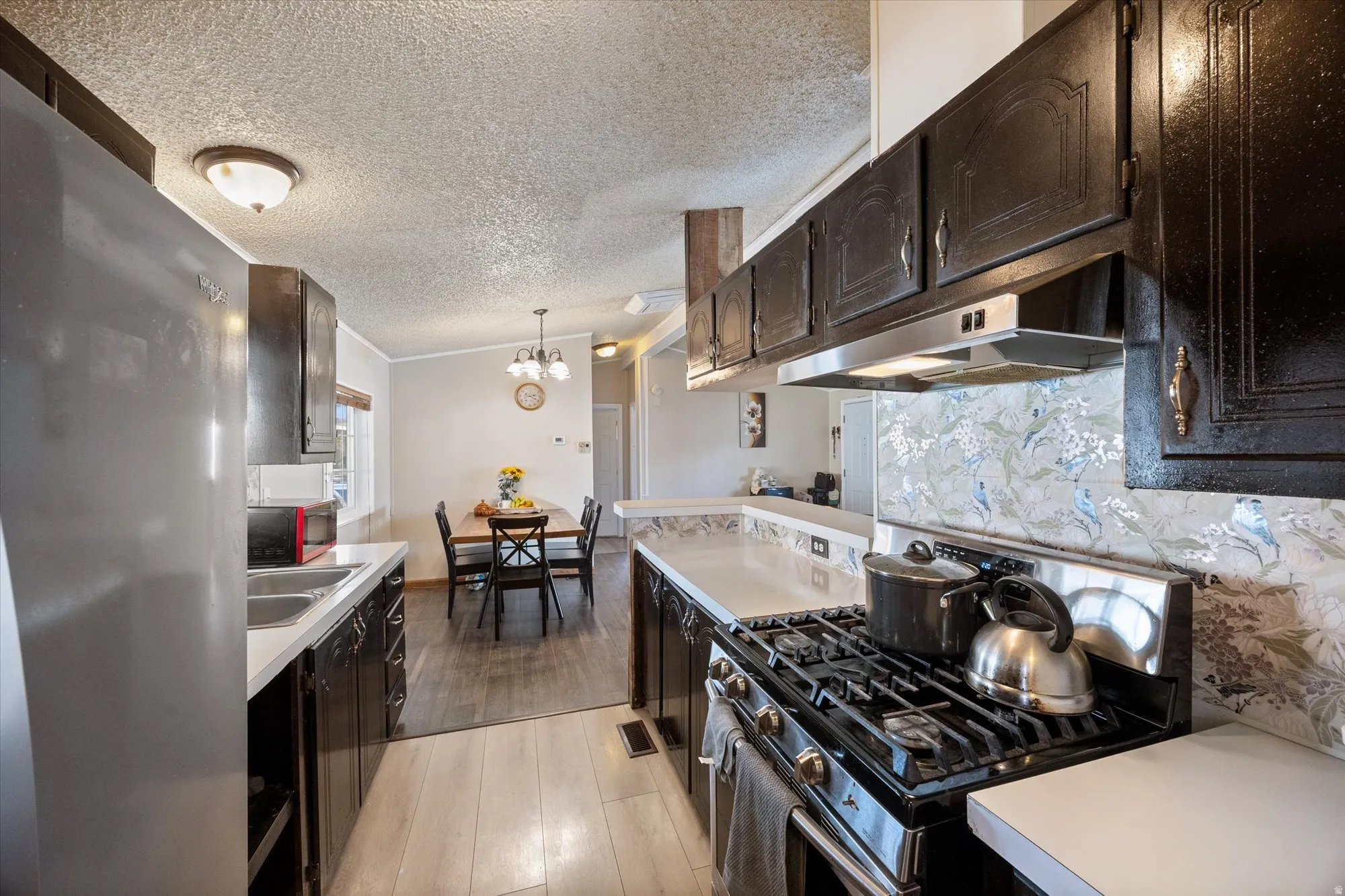 Kitchen featuring appliances with stainless steel finishes, light countertops, light wood-type flooring, pendant lighting, and under cabinet range hood