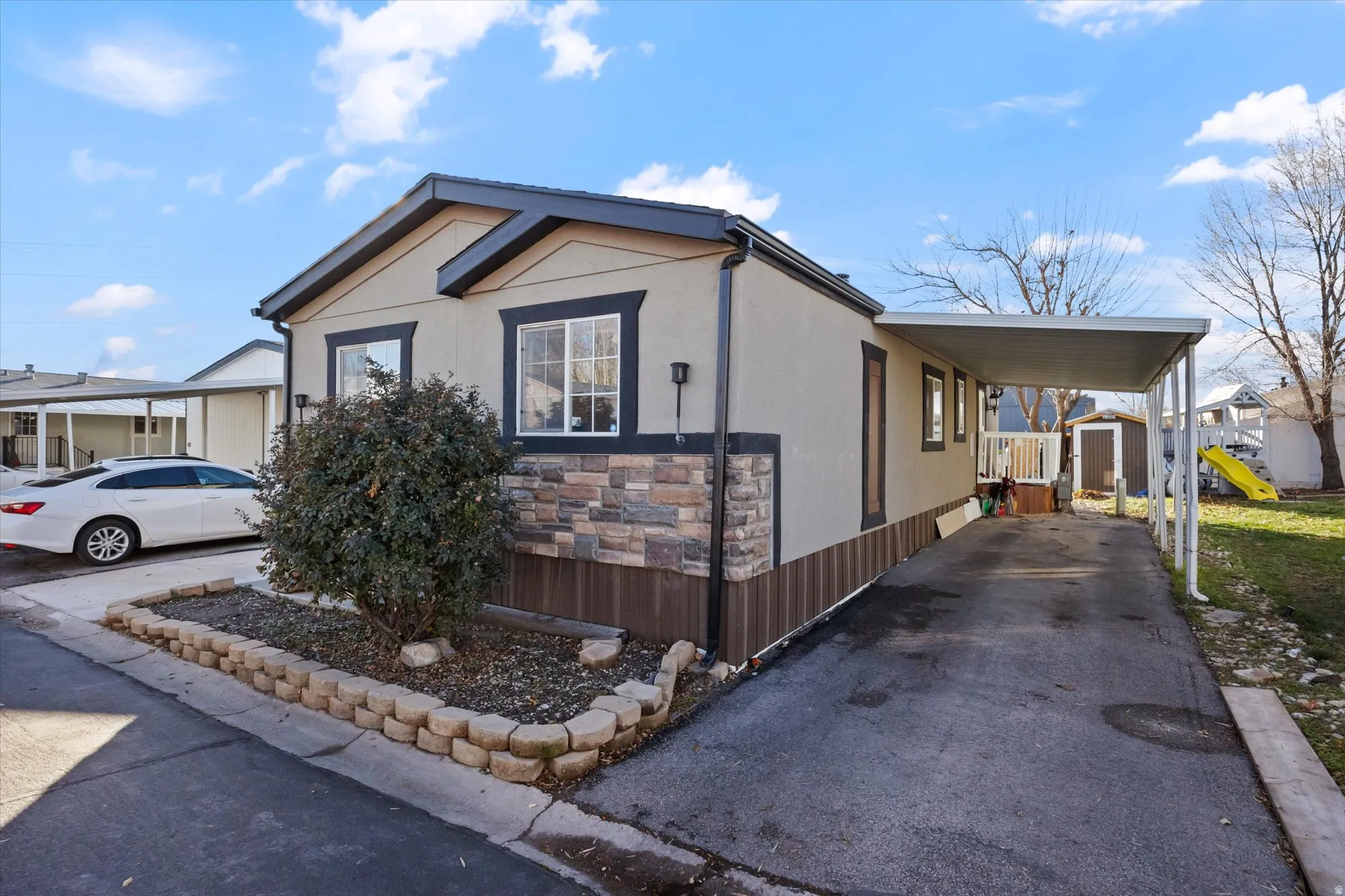 View of side of property with stone siding, a storage shed, stucco siding, an attached carport, and asphalt driveway