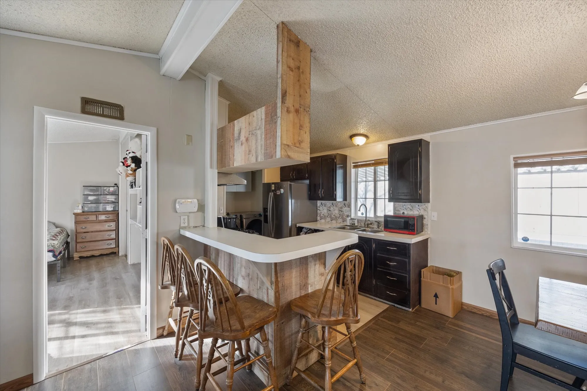 Kitchen with light countertops, dark wood-type flooring, a kitchen breakfast bar, a textured ceiling, and stainless steel fridge with ice dispenser
